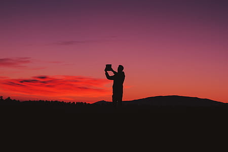silhouette of person standing on mountain under red sky thumbnail