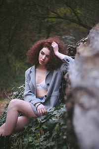 selective focus photo of woman wearing gray button-up coat sitting on grass covered rock thumbnail