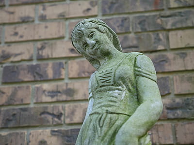 Stone statue of a woman in front of a wall of bricks thumbnail