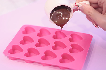 person pouring chocolate in pink heart shape molding tray thumbnail