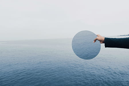 person holding round mirror beside body of water thumbnail