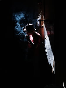 man smoking cigarette standing near gray wall inside dark room thumbnail