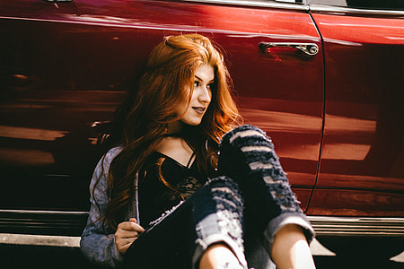 smiling woman sitting on floor while leaning on red vehicle during daytime thumbnail