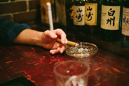 person holding lighted tobacco beside round clear glass ashtray thumbnail