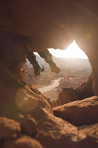 person wearing black leather boots sitting on brown rock formation near highway during daytime thumbnail