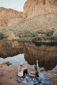 Two Woman Sitting on Blue Blanket Facing Rock Cliff thumbnail