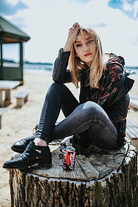 Beautiful blonde woman relaxing with a can of coke on a tree stump by the beach thumbnail