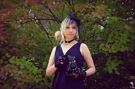 woman holding black camera near tree thumbnail