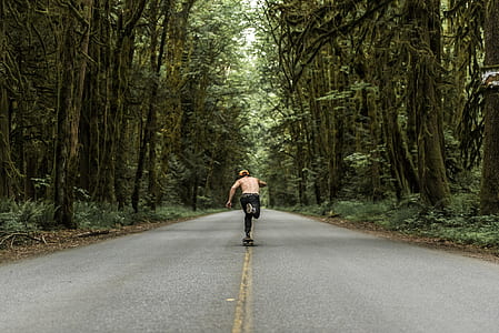 man playing skateboard on road between forest thumbnail