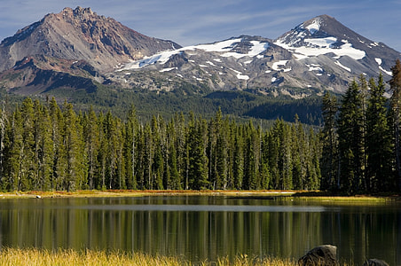 lake surrounded by evergreen trees near snowy mountain during daytime thumbnail