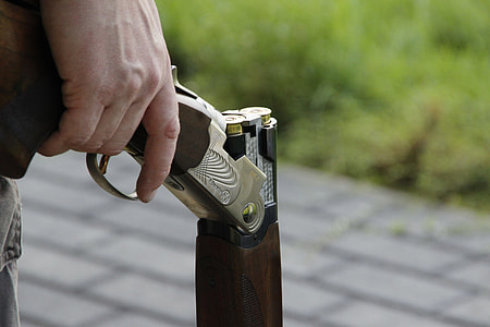 person standing on concrete pavement near grass field while holding lever action rifle during daytime thumbnail
