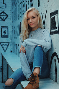 woman in sweatshirt, distressed jeans, and brown lace-up boots sitting with forearm resting on left lap thumbnail