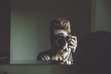 man taking photo using black camera through mirror thumbnail