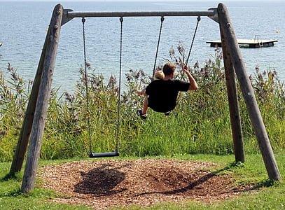 man in black shirt riding swing during daytime thumbnail