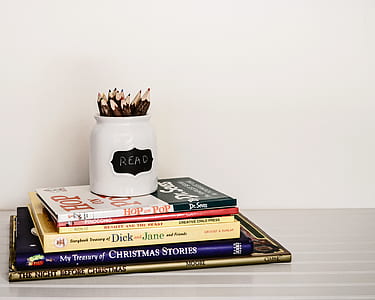 white and black ceramic pen case on stack of assorted-title books thumbnail