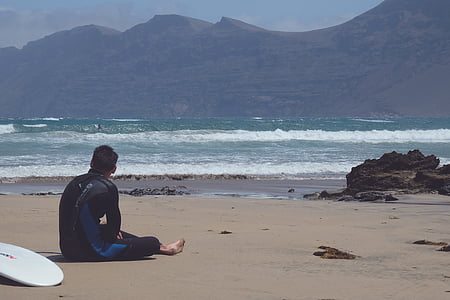 man wearing wetsuit sitting on seashore thumbnail