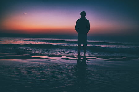 man standing in front of ocean at golden hour thumbnail