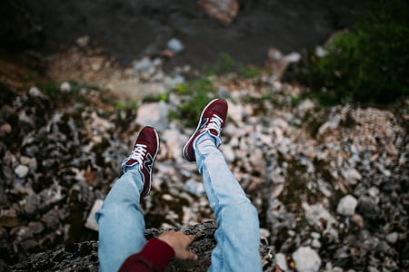 person wearing maroon sneakers sitting on top of gray rock fragment thumbnail