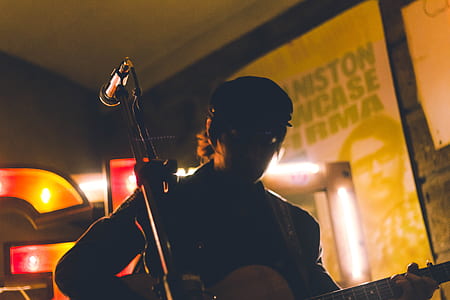 silhouette of man playing guitar on stage beside microphone in room thumbnail