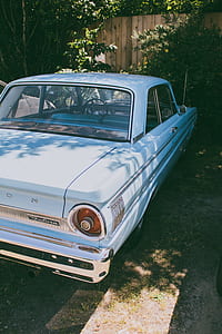 white coupe parked ahead in front of green plants thumbnail