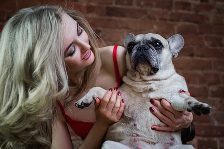 woman wearing red spaghetti strap top carrying French bulldog thumbnail