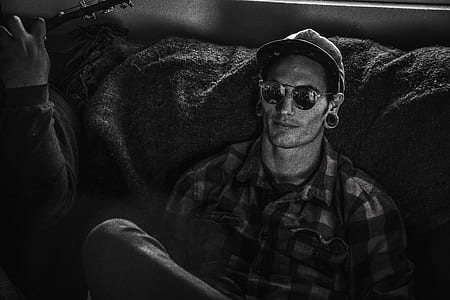 Grayscale Photo of Man Wearing Snapback Cap and Plaid Dress Shirt Sitting on Couch thumbnail