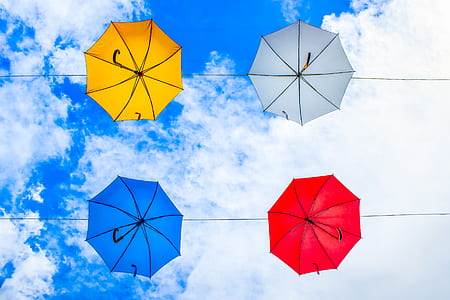 four hanged blue, yellow, white, and red umbrellas taken under white clouds during daytime thumbnail