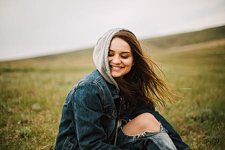 panning photography of female wearing blue denim hoodie while sitting on green grass field thumbnail