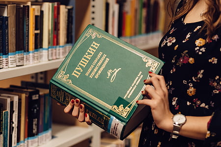 woman holding and opening book in front of book lot on shelves thumbnail