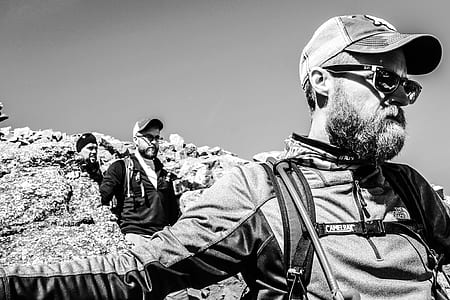grayscale photography of three men hiking on rock formation thumbnail