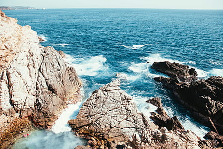 Natural rock pools by the ocean with waves crashing on rocks in sunshine thumbnail
