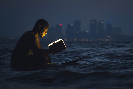 Man reading a book in the ocean at night thumbnail