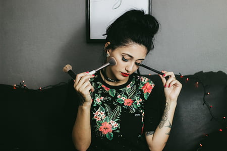 woman holding makeup brush while sitting on black sofa thumbnail