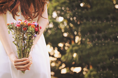 woman holding white dress while holding a red, purple and red flowers thumbnail