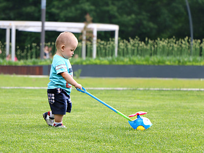 boy wearing blue crew-neck shingle holding learning walker toy standing on green grass during daytime thumbnail