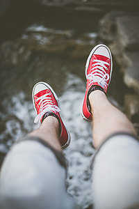 selective focus photography of man's feet wearing red lace-up low-top sneakers above body of water thumbnail