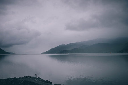 silhouette of mountain near body of water during foggy day thumbnail