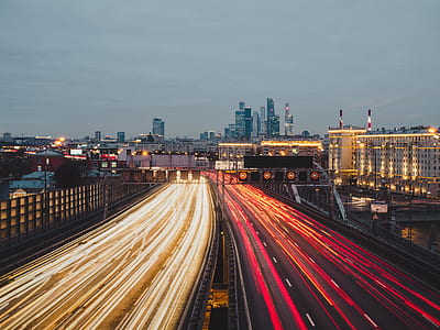 time lapse photography of road near concrete buildings under gray sky at nighttime thumbnail