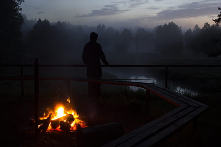 person looking into body of water with bonfire behind him thumbnail