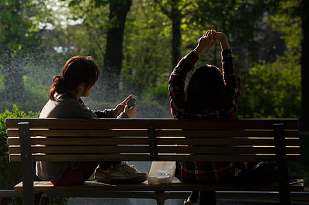 two woman sitting on bench in front of trees thumbnail