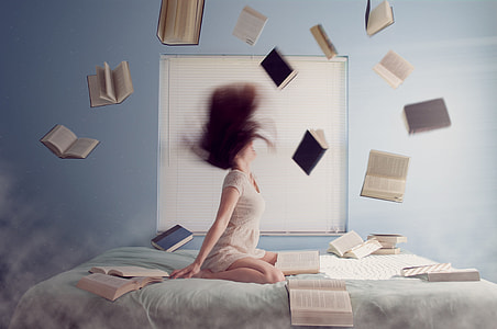 woman in white dress throwing assorted books while whipping her hair on bed thumbnail