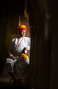 man wearing thobe and turban sitting beside window thumbnail