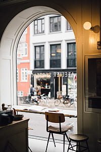 brown and black armless chair and round stool beside glass frame near white building and road at daytime thumbnail