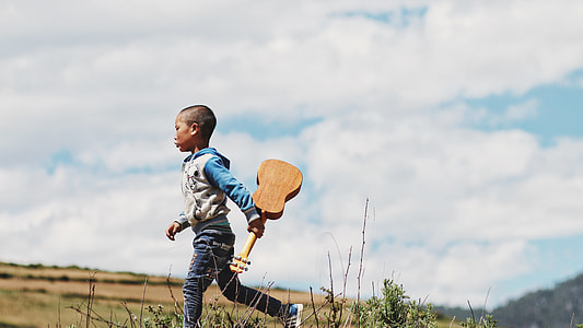 boy holding guitar running during daytime thumbnail