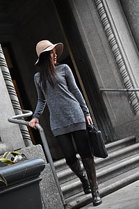 woman in gray sweater and black leggings holding handbag walking downstairs thumbnail