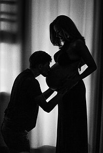 man wearing black crew-neck shirt kissing woman pregnant belly thumbnail