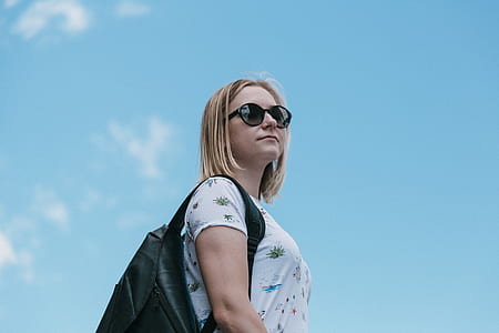 low-angle photography of woman wearing sunglasses and white shirt while carrying backpack under clear blue sky thumbnail