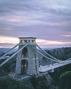 gray concrete suspension bridge near forest under cloudy sky at sunset thumbnail