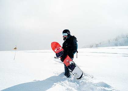 person carrying red and white snowboard standing on snow field taking pose for a photo thumbnail