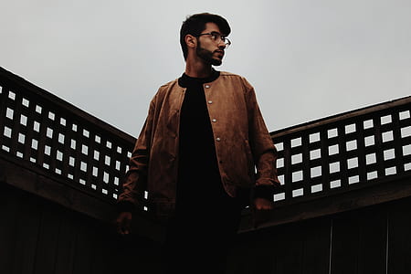 man in brown button-up jacket leaning on brown wooden railings thumbnail